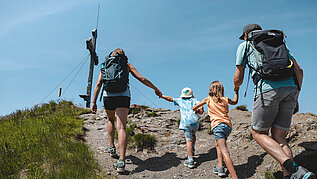 Familie mit zwei Kindern auf dem letzten Weg zum Gipfelkreuz im Wanderurlaub in Tirol.