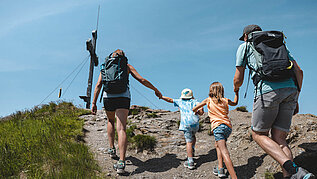 Familie mit zwei Kindern auf dem letzten Weg zum Gipfelkreuz im Wanderurlaub in Tirol.