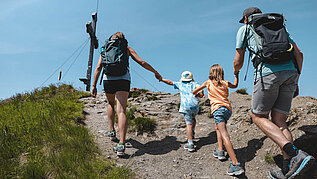 Familie mit zwei Kindern auf dem letzten Weg zum Gipfelkreuz im Wanderurlaub in Tirol.