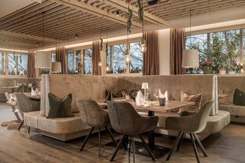 Gemütlicher Restaurantbereich im Familienhotel Mia Alpina in Tirol mit gedecktem Tisch, Sitzbank, Stühlen, Kinderhochstuhl und warmem Licht.