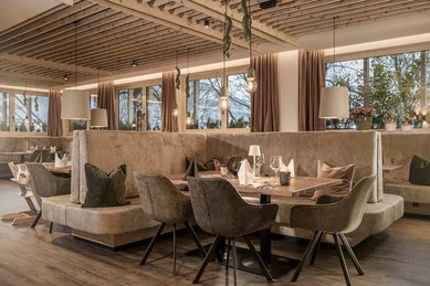 Gemütlicher Restaurantbereich im Familienhotel Mia Alpina in Tirol mit gedecktem Tisch, Sitzbank, Stühlen, Kinderhochstuhl und warmem Licht.