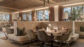 Gemütlicher Restaurantbereich im Familienhotel Mia Alpina in Tirol mit gedecktem Tisch, Sitzbank, Stühlen, Kinderhochstuhl und warmem Licht.