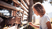 Ein Mädchen füttert eine Ziege mit Gras im Gehege im Familienhotel Family Home Alpenhof.