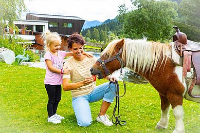Mutter und Tochter füttern ein Pony im Familienhotel Alphotel Tyrol Wellness & Family Resort in Südtirol.
