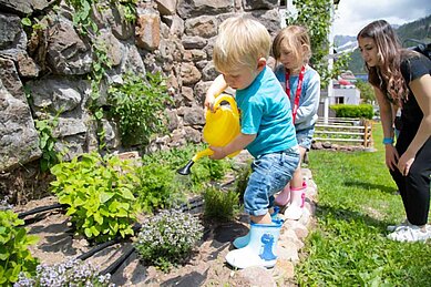 Kleiner Junge gießt die Kräuter im Garten vom Familienhotel Engel Gourmet & Spa in Südtirol.
