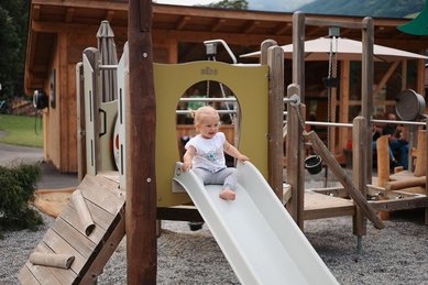 Ein kleines Mädchen auf der Rutsche auf dem Spielplatz am Familienhotel Habachklause im Salzburger Land 