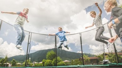 Mehrere Kinder springen auf einem Trampolin im Außenbereich des Familienhotels Landgut Furtherwirt in Tirol.