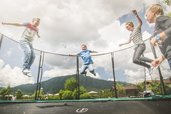 Mehrere Kinder springen auf einem Trampolin im Außenbereich des Familienhotels Landgut Furtherwirt in Tirol.