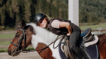 Ein Kind reitet auf einem Pony im Außenbereich des Familienhotels Oberkarteis im Salzburger Land.