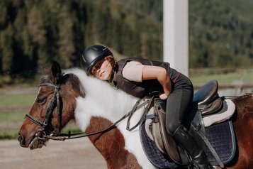 Ein Kind reitet auf einem Pony im Außenbereich des Familienhotels Oberkarteis im Salzburger Land.