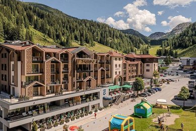 Familienhotel Zauchenseehof im Sommer mit Blick auf das modernisierte Gebäude und den angrenzenden Spielbereich vor der Bergkulisse.