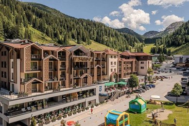 Familienhotel Zauchenseehof im Sommer mit Blick auf das modernisierte Gebäude und den angrenzenden Spielbereich vor der Bergkulisse.
