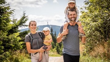 Eine Familie wandert nahe dem Familienhotel Elldus Resort im Erzgebirge mit Baby, Kind auf den Schultern und Blick ins Grüne.