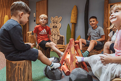 Kinder spielen am unechten Lagerfeuer aus Holz in der Happy World des Familienhotels Huber in Südtirol.