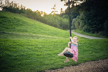 Kleines Mädchen schaukelt auf dem Flying Fox auf dem Außenspielplatz des Familienhotels Schreinerhof im Bayerischen Wald.