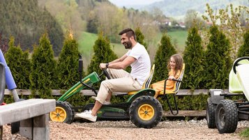 Vater fährt lachend mit seiner Tochter im Doppelsitzer-Kettcar durch das Außengelände eines Familienhotels