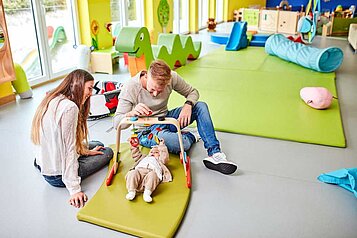 Eltern spielen mit ihrem Baby im Babyzimmer im Familienhotel Aigo welcome family in Oberösterreich.