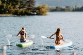 Zwei Kinder paddeln im Sommer auf dem See mit SUP-Boards beim Familienhotel Amiamo vor malerischer Bergkulisse.