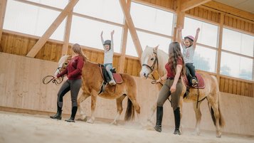 Reiten mit Spaß: Zwei Kinder zeigen stolz ihre Balanceübungen im Familienhotel Friedrichshof.