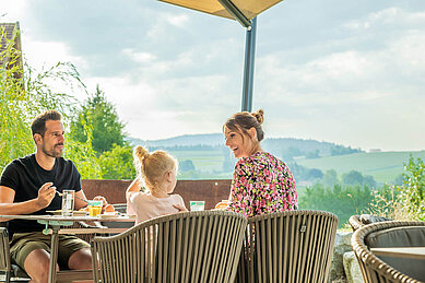 Familie sitzt auf der Terrasse des Familienhotels Schreinerhof und genießt ihr Frühstück in der Sonne.