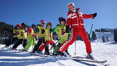 Der Ski Lehrer fährt vor den Kinder den Berg runter.