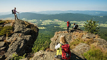 Wanderer stehen im Bayerischen Wald an einer Klippe des Kaitersberges und genießen die Aussicht.