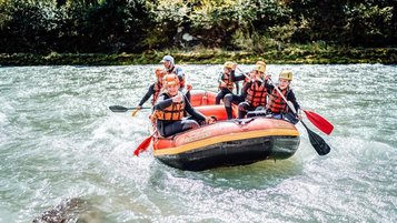 Teens fahren beim Familienhotel Amiamo im Salzburger Land mit Helm und Schwimmweste beim Wildwasser Rafting über einen Fluss.