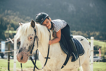 Kleiner Junge sitzt auf dem Pferd und umarmt es im Familienhotel Post Family Resort im Salzburger Land.