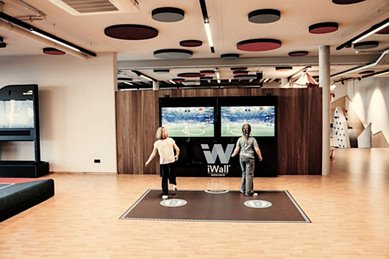Innenbereich der Fun Company im Familienhotel Mia Alpina in Tirol mit Kindern auf einem Spielteppich iWall und großem Fernseher.