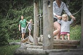 Eine Familie balanciert im Wald über Holzstämme im Familienhotel Alphotel Tyrol Wellness & Family Resort in Südtirol.