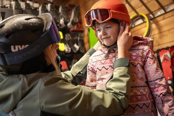 Im Skiverleih des Familienhotels Elldus im Erzgebirge hilft ein Ski-Lehrer beim Anpassen des Helms für das Kind.
