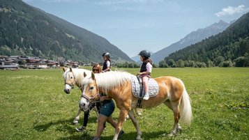Kinder reiten auf Haflingern durch eine idyllische Wiese im Familienhotel Kindl.