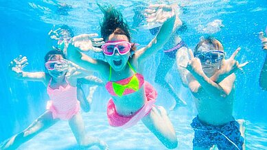 Drei Kinder tauchen unter Wasser und lachen im Pool des Familienhotels Landhaus zur Ohe.