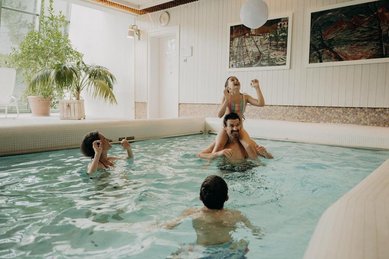 Eine Familie badet im Hallenbad des Hotel Sonngastein im Salzburger Land mit hellem Poolbereich und großen Fenstern.