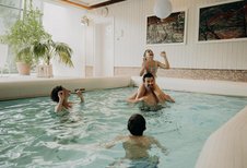 Eine Familie badet im Hallenbad des Hotel Sonngastein im Salzburger Land mit hellem Poolbereich und großen Fenstern.