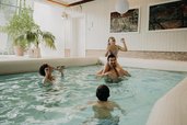 Eine Familie badet im Hallenbad des Hotel Sonngastein im Salzburger Land mit hellem Poolbereich und großen Fenstern.