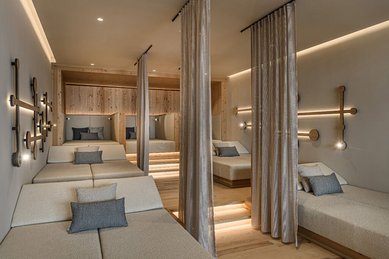 Ruhiger Ruheraum im Zauchenseehof mit gepolsterten Liegen, halbtransparenten Vorhängen und sanfter, indirekter Beleuchtung in warmem Holzambiente.