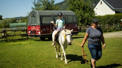 Ein Kind reiten auf einem kleinen weißen Pferd.