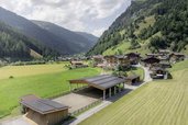 Mehrere Gebäude des Familienhotels Oberkarteis im Salzburger Land sind aus der Vogelperspektive mit einem teilweise überdachten Sandplatz zum Reiten vor Wiesen und Bergen zu sehen.