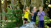 Drei Jungs beim Bogenschiessen mit selbstgebastelten Pfeil und Bogen im Familienhotel Sonne Bezau.