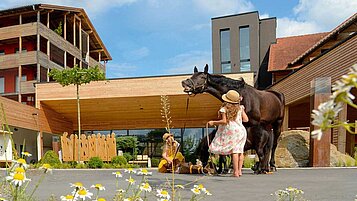 Zwei Mädchen stehen mit einem Pferd vor dem Eingang des Familienhotels Ulrichshof im Sommer.