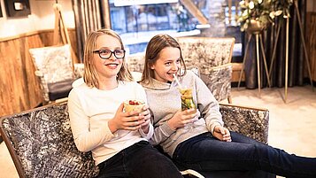 Zwei Teenager sitzen auf einer Couch und trinken alkoholfreie Cocktails