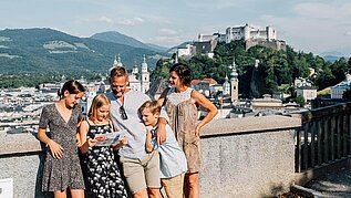 Familie steht in der Salzburger Altstadt, im Hintergrund zu sehen ist die Festung.