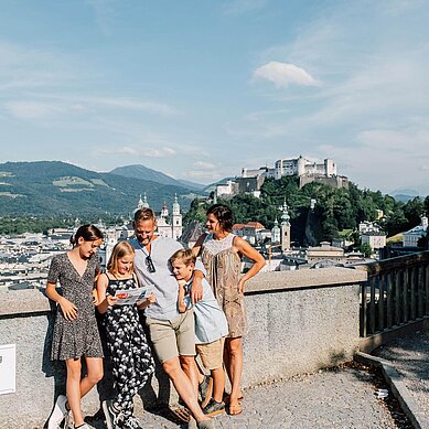 Familie steht in der Salzburger Altstadt, im Hintergrund zu sehen ist die Festung.