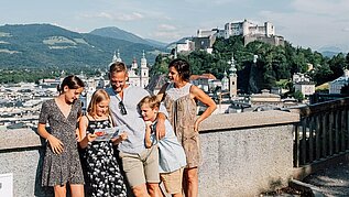 Familie steht in der Salzburger Altstadt, im Hintergrund zu sehen ist die Festung.