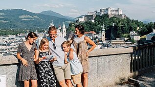 Familie steht in der Salzburger Altstadt, im Hintergrund zu sehen ist die Festung.