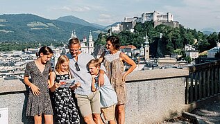 Familie steht in der Salzburger Altstadt, im Hintergrund zu sehen ist die Festung.