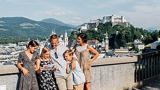 Familie steht in der Salzburger Altstadt, im Hintergrund zu sehen ist die Festung.