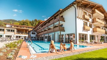 Mutter sitzt mit ihren beiden Kindern in Badekleidung am Beckenrand des Außenpools im Familienhotel Das Bayrischzell.