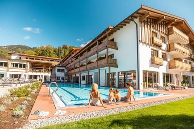 Mutter sitzt mit ihren beiden Kindern in Badekleidung am Beckenrand des Außenpools im Familienhotel Das Bayrischzell.
